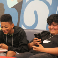 students at the library look at their phones while smiling