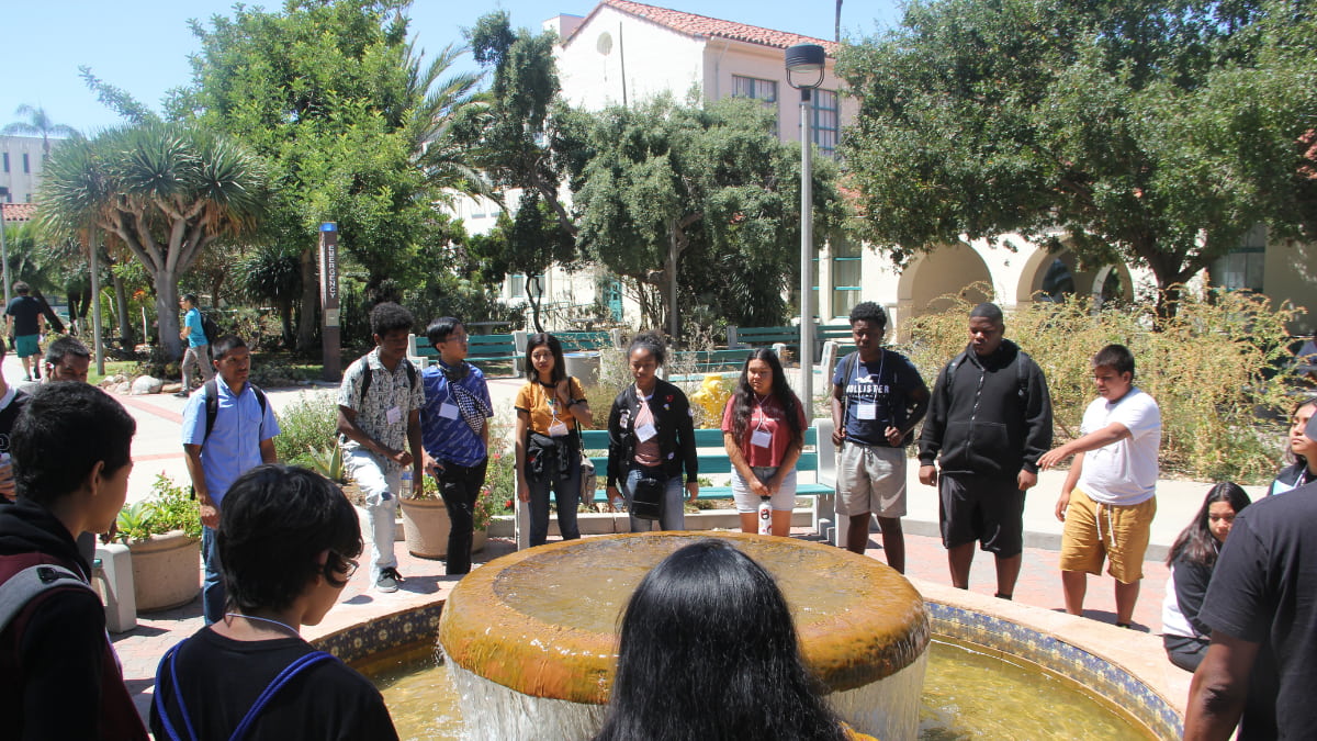 A group of students circle a water fountain.